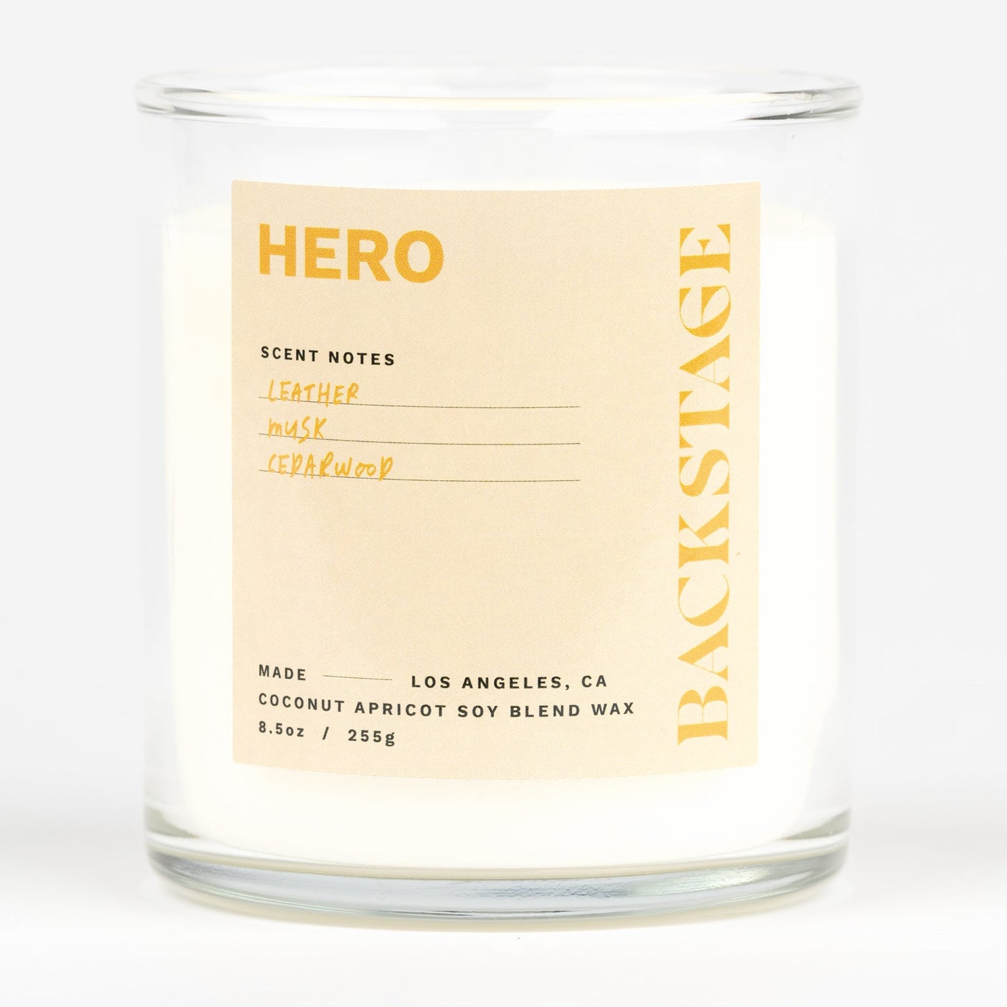 A white candle labeled 'HERO' with a scent description that includes cucumber, mint, cardamom, iris, violet, sandalwood, cedarwood, and warm spices.