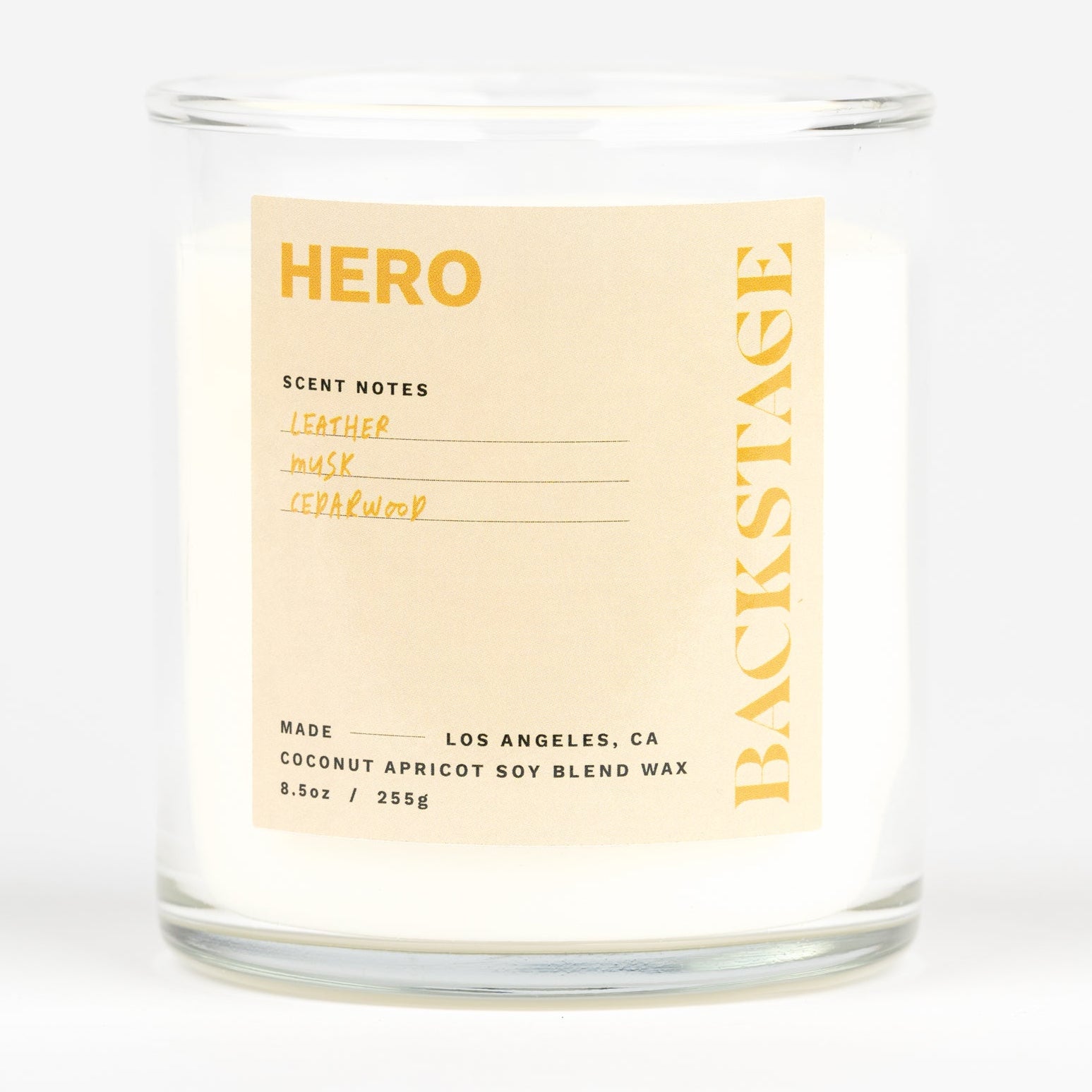 A white candle labeled 'HERO' with a scent description that includes cucumber, mint, cardamom, iris, violet, sandalwood, cedarwood, and warm spices.