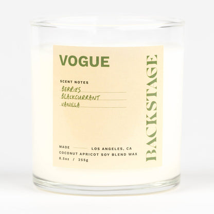 A white candle jar with the label 'VOGUE' on it, indicating the scent of the candle.
